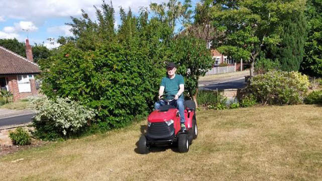 A man using a 1330m mountfield riding a lawn mower to cut grass