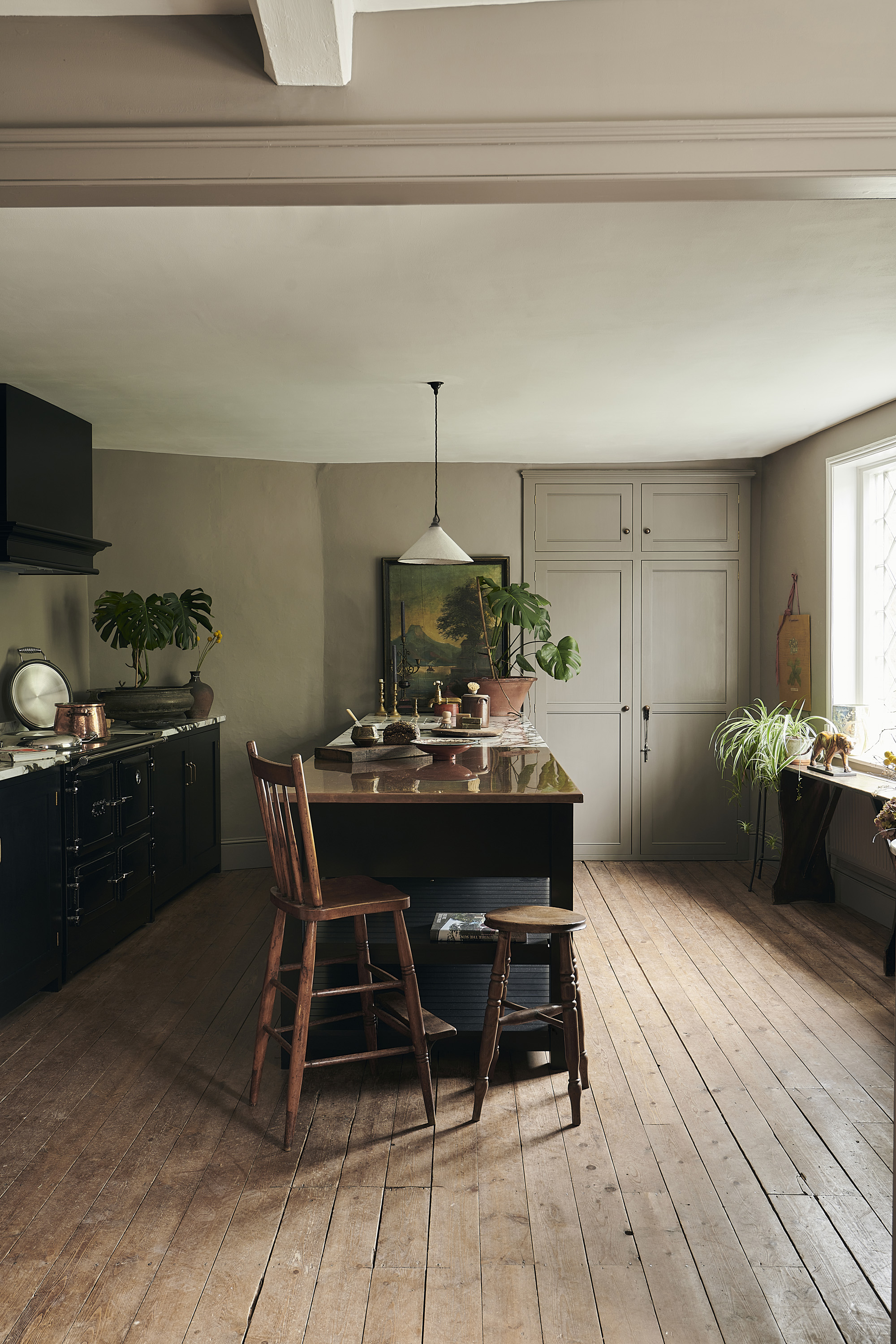 A kitchen with wooden flooring, black-painted cabinets and wooden chairs