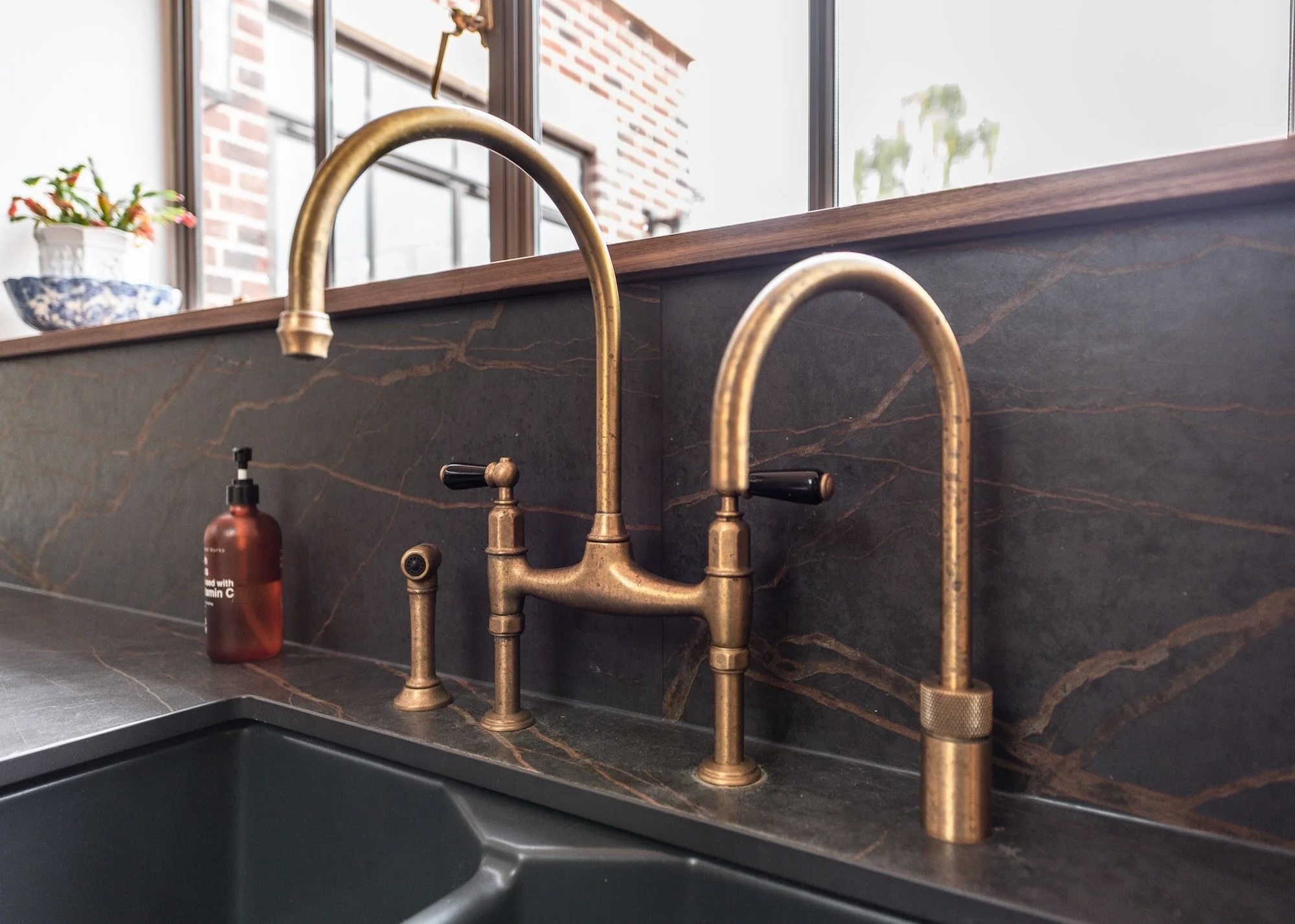 a kitchen sink showing a swan neck tap in a brushed brass finish, a separate boiling water tap and separate pull out rinse