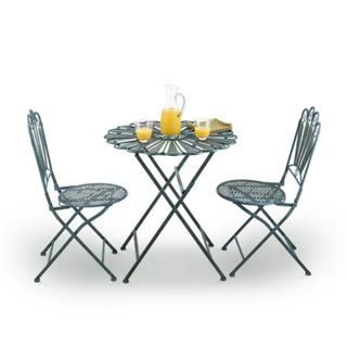 Two teal blue outdoor patio chairs with scalloped backs with a flower shaped teal blue table in the middle with a jug and two glasses of orange juice