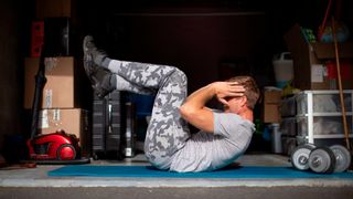 Man performs crunch exercise in a garage, dumbbells on the floor next to him