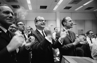 On April 17, 1970, NASA staff members, including NASA Administrator Thomas Paine (center), celebrate a successful Apollo 13 splashdown from inside the Mission Control Center of NASA's Manned Spacecraft Center in Houston. On the right, George Low, manager of the Apollo spacecraft program, smokes a cigar.