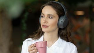 Edifier W820NB Plus worn by a woman, holding a coffee cup outside