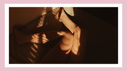 Picture of a women's legs as she lies on a bed with orange sheets/ in a pink template