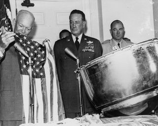 President Dwight D. Eisenhower examines the first American flag flown and returned from Earth orbit on the Discoverer XIII reentry capsule during an Aug. 15, 1960 ceremony at the White House in Washington, D.C.