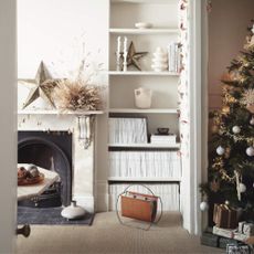 Beige living room with fireplace and shelving, next to a christmas tree with presents underneath it