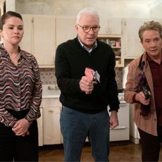 Selena Gomez as Mabel, Steve Martin as Charles (holding a pink nail gun), and Martin Short as Oliver (holding a gun), standing in a pre-war apartment kitchen, in 'Only Murders in the Building' season 4.