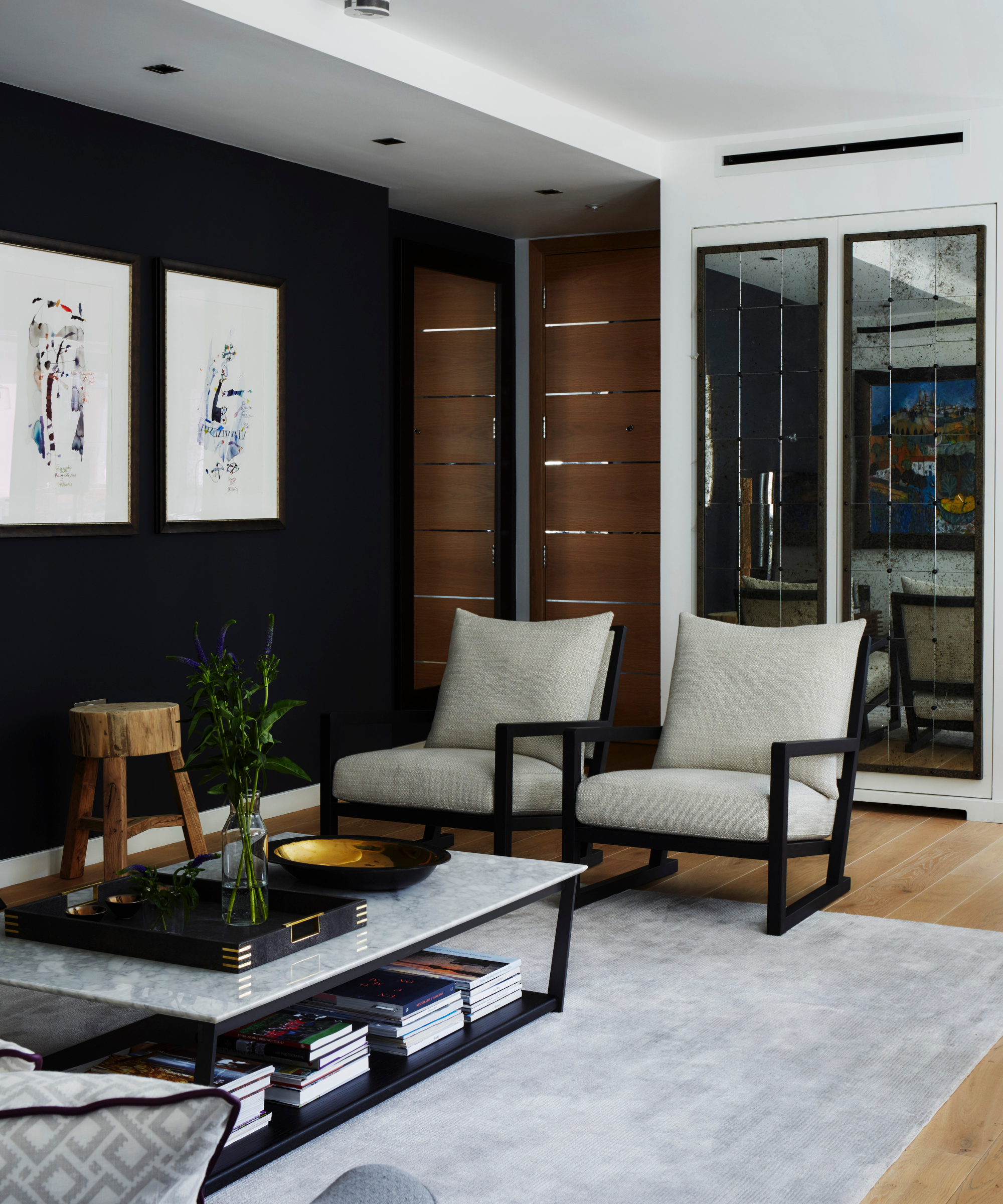 a modern sitting room with two chairs, a marble coffee table, a gray rug, and a black wall with art hanging on it