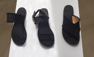 Three different shaped black woman's sandals on a white surface.
