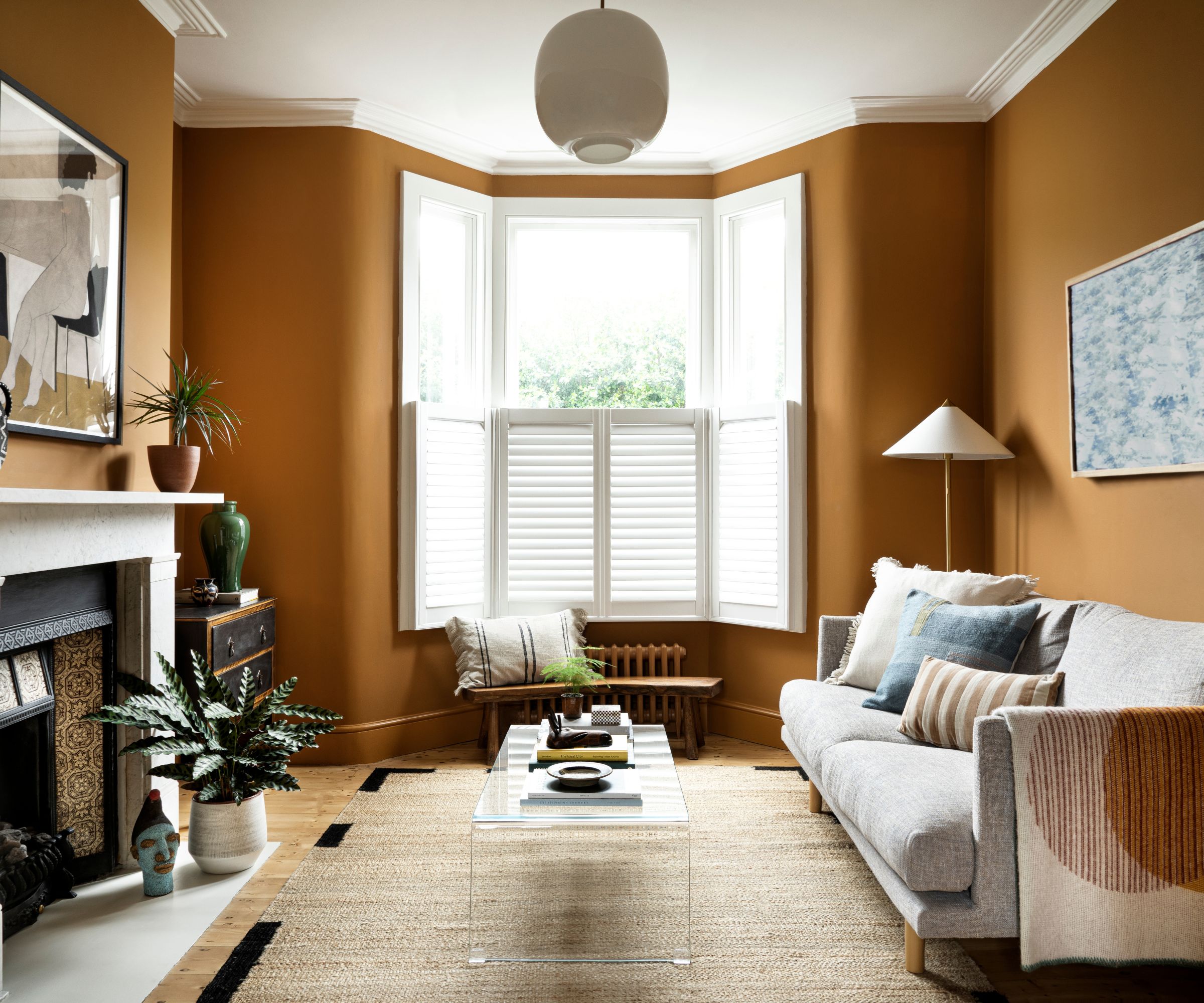 living room with dark orange walls and modern neutral decor with white shutters on bay window