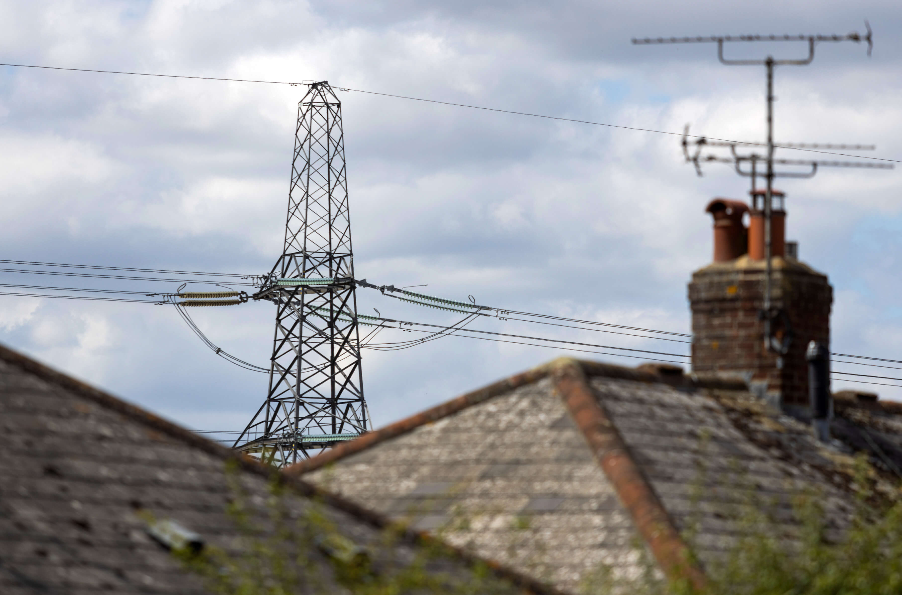 An electricity transmission tower and rooftops under a cloudy sky