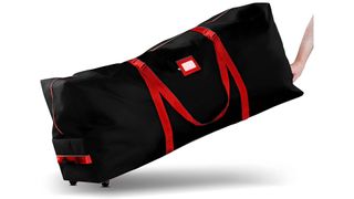 A person's hand pulling a black rolling Christmas tree storage bag with red handles, for the best Christmas tree storage bags.