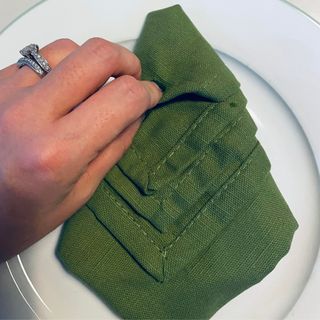 Tucking the tips in of a green napkin on a white plate