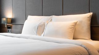 Two pairs of white pillows propped up against the headboard in a brightly lit hotel bedroom