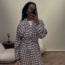 A woman wearing a plaid trench coat and blue jeans