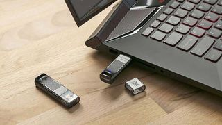 A SanDisk USB flash drive plugged into the USB port of a laptop sitting next to another SanDisk USB flash drive