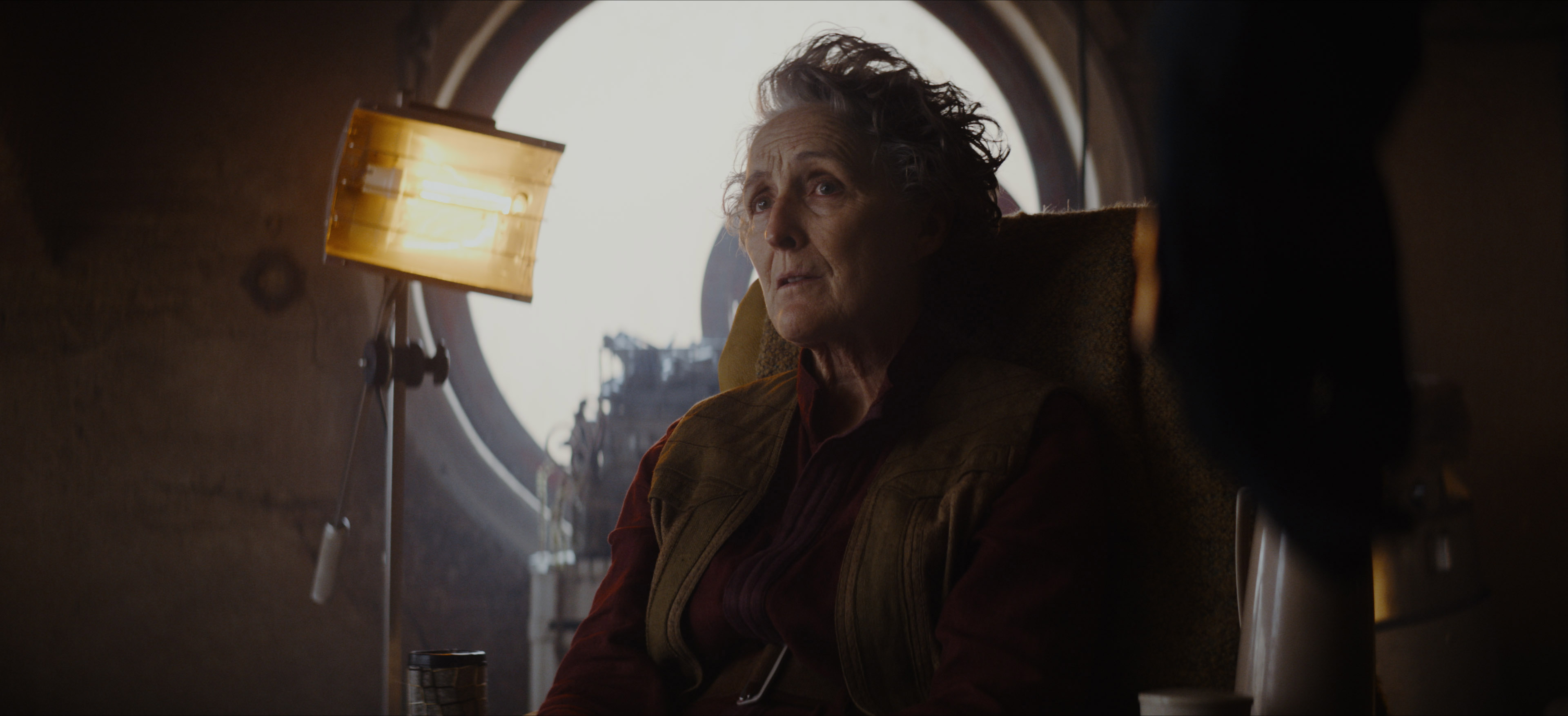Fiona Shaw as Maarifa, sitting on a chair in Andor