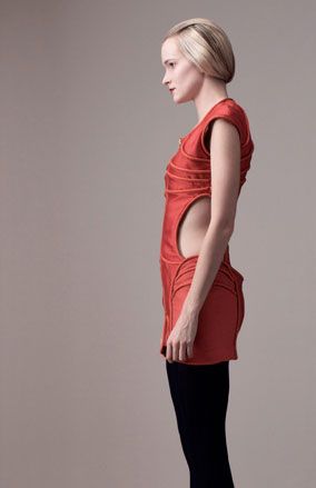 Young female model, side view to the camera, wearing a red Odysee dress by Ara fashion, navy blue tights, pale grey background