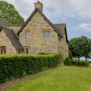 A countryside house with a hedge and a green field
