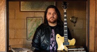 Wolfgang Van Halen sits in a hotel/motel reception with his buttercream signature EVH electric guitar