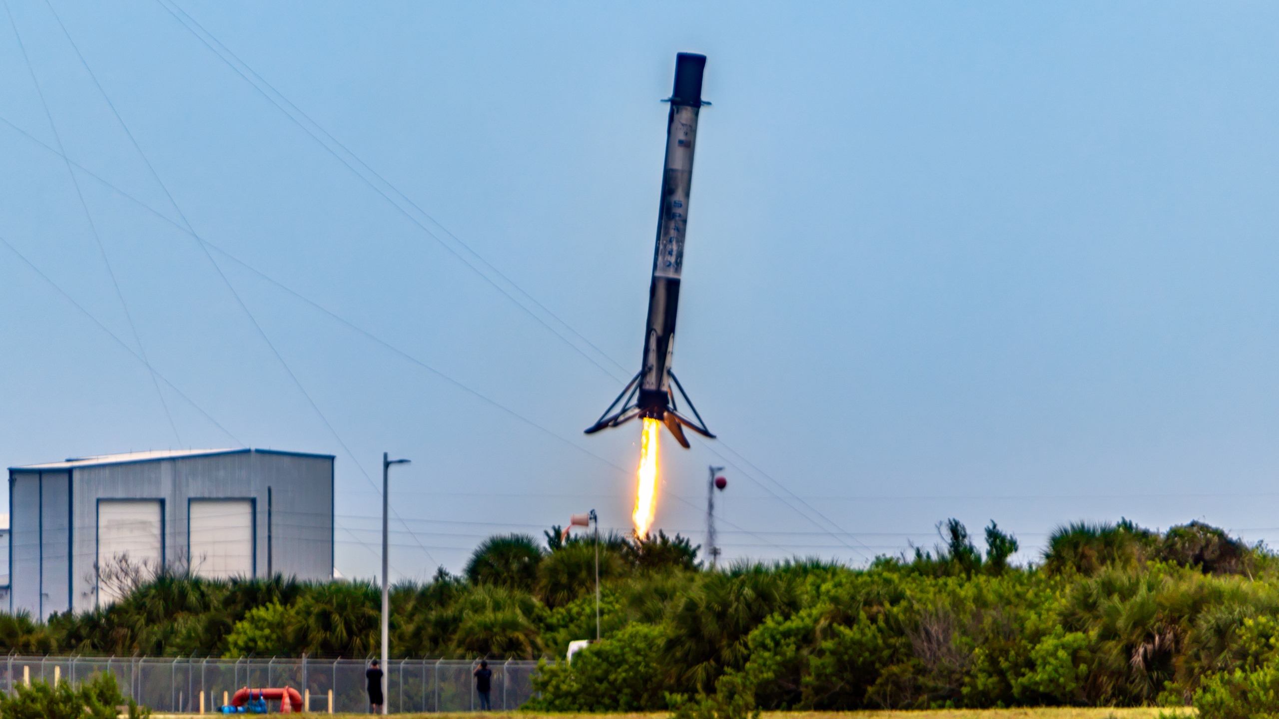 A sooty first stage Falcon 9 rocket booster performs a landing burn as its legs deploy.
