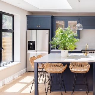 kitchen. beside a window with a tall chrome fridge freezer and bar stools around a kitchen island