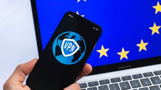 Hand with mobile phone and VPN application with the EU flag on a laptop's screen on the background