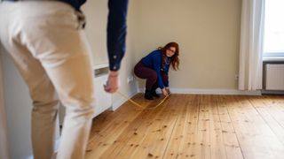 Women measuring flooring with tape measure in house
