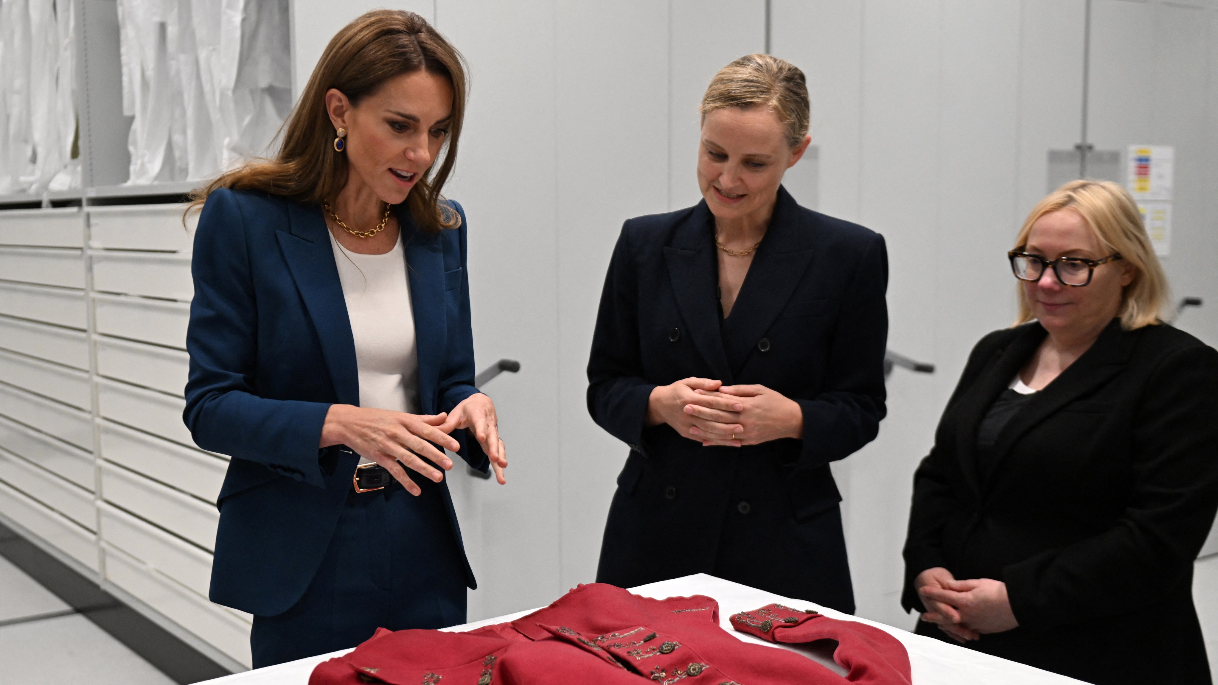 Catherine, Princess of Wales talks with Senior Fashion and Textiles Curator, Oriole Cullen, and Director of Collections Care and Access, Kate Parsons, as she is shown a 19th Century Riding Habit, during a visit to the V&A East Storehouse