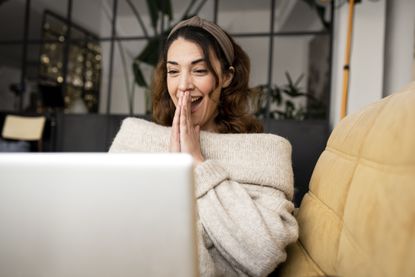 Excited woman looking at a laptop sitting on a sofa at home