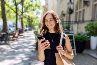 A smiling woman walk down the street whilst using her smartphone