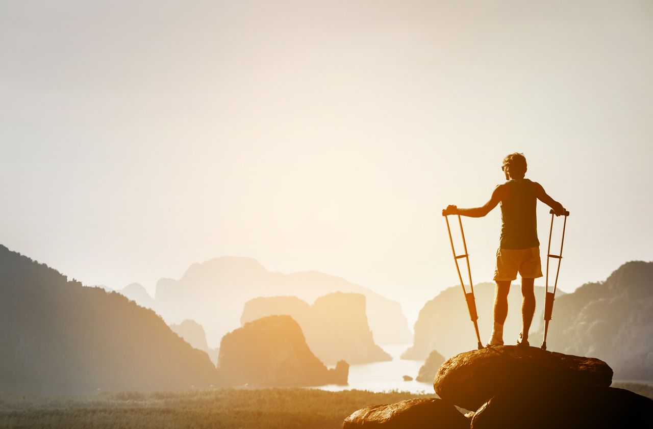 Disabled man with crutches stands on a big rock and looking at great view to islands and mountains. Space for text. Winner pose