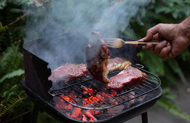 Someone searing steaks on a smoky BBQ.