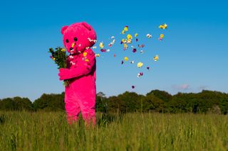 Pink bear with flower petals blowing in the wind