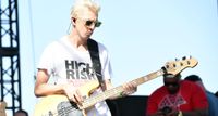 A bleached-blond Stu "Bassie" Brooks wears shades and plays bass in the bright sunshine.