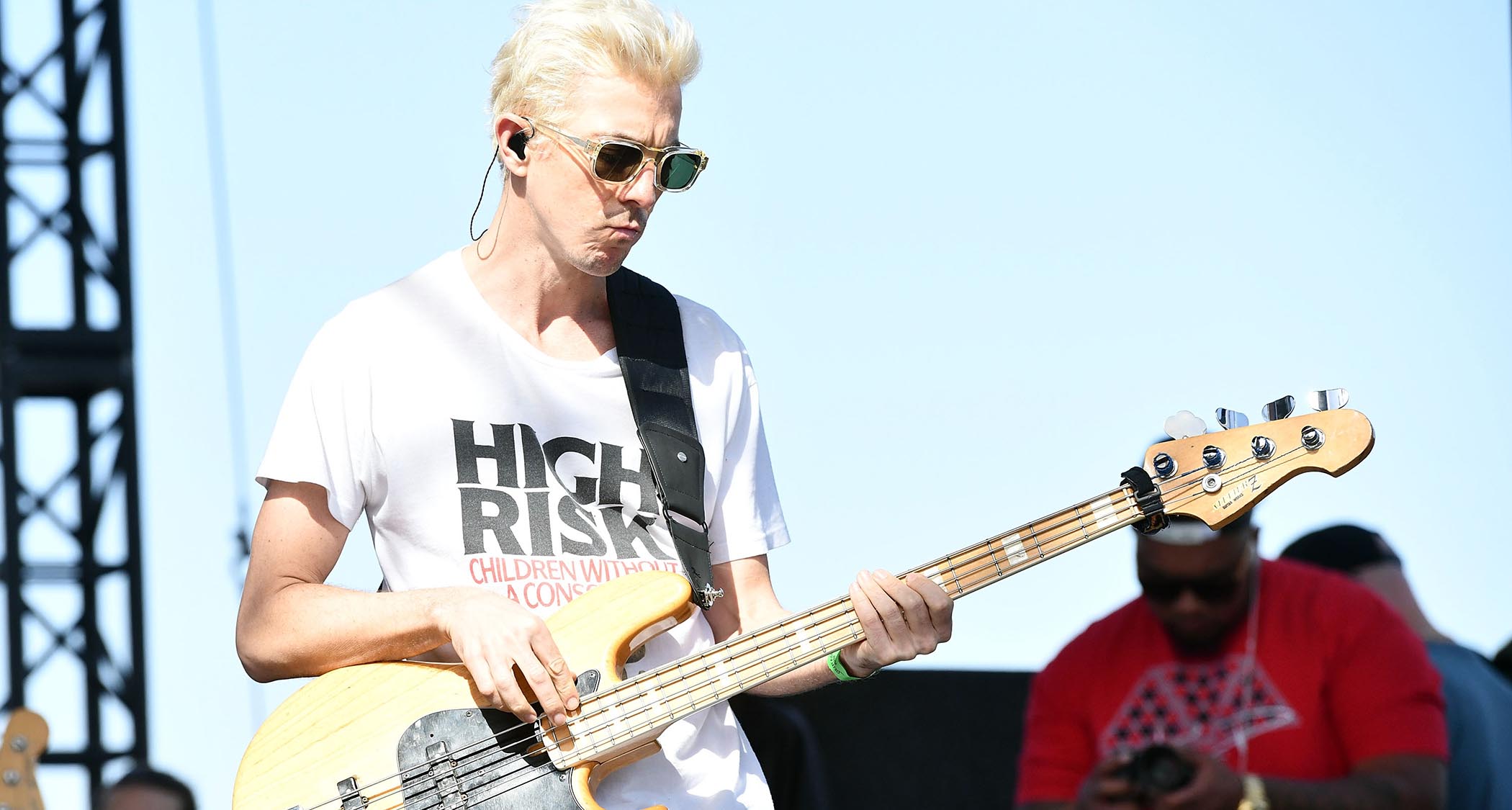 A bleached-blond Stu "Bassie" Brooks wears shades and plays bass in the bright sunshine.