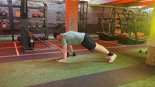 Personal trainer at Gymbox Aaron Cook performing plank dumbbell pull throughs