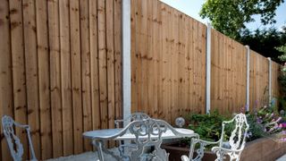 Wooden fence panels with concrete posts and furniture in the foreground