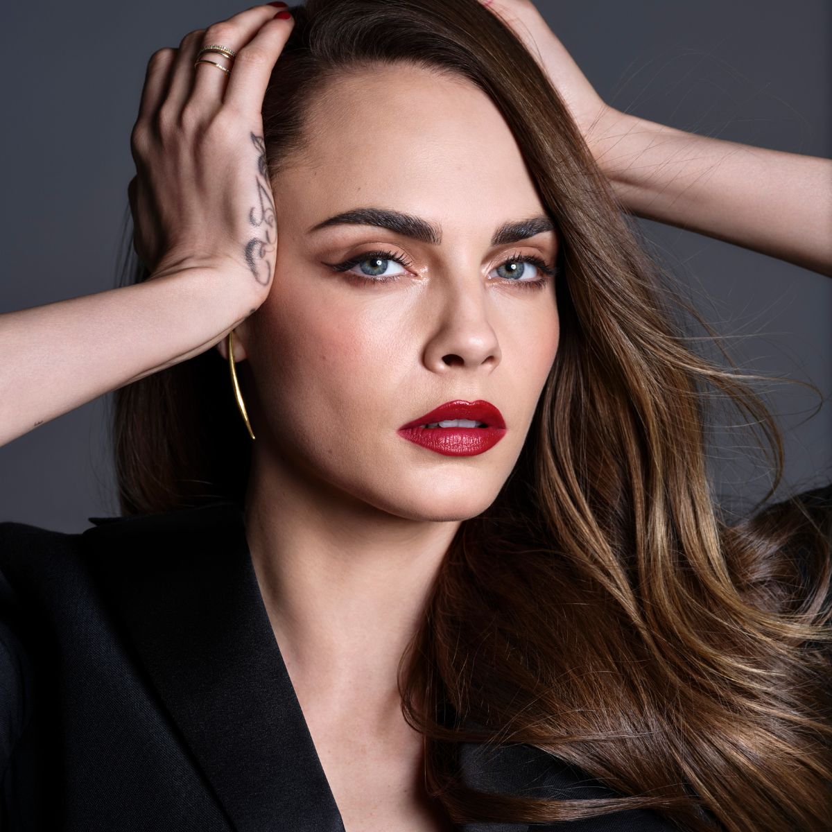An image of Cara Delevingne wearing red lipstick and winged eyeliner against a gray backdrop.