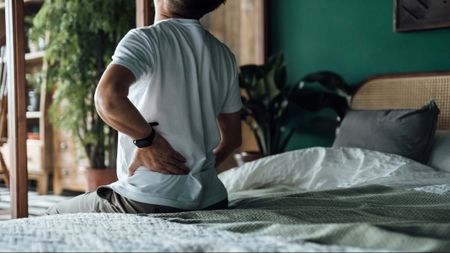 Man sitting on the edge of his bed holding his back in pain