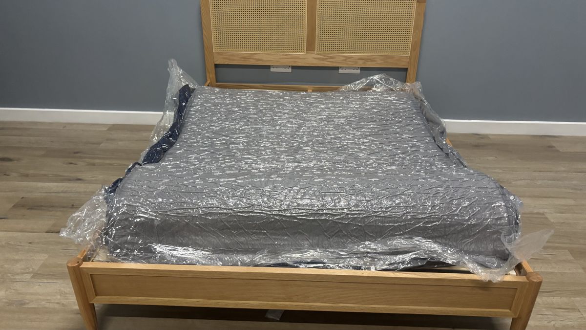 The unboxed but still compressed SweetNight CoolNest Mattress wrapped in plastic and spead out on a wooden bed frame.