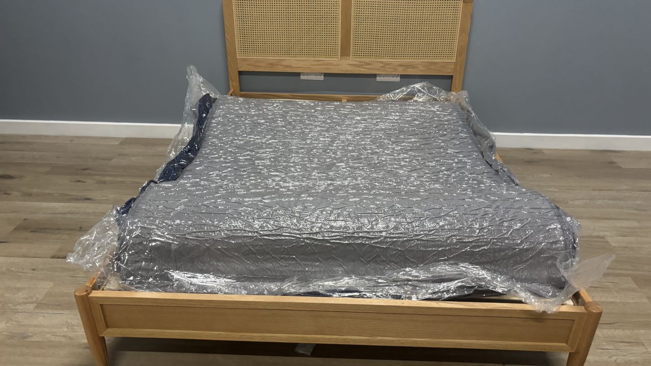 The unboxed but still compressed SweetNight CoolNest Mattress wrapped in plastic and spead out on a wooden bed frame.
