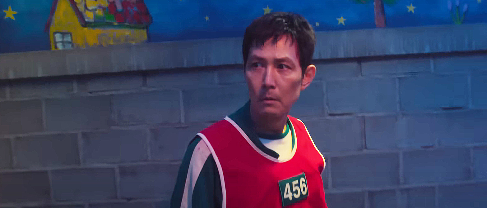 Seong Gi-hun wearing his green jumpsuit and a red bib with 456 on it in Squid Game season 3