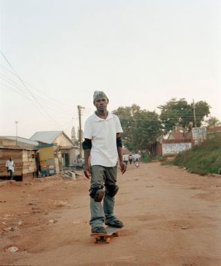 An African man standing on a skateboard on a sand road.