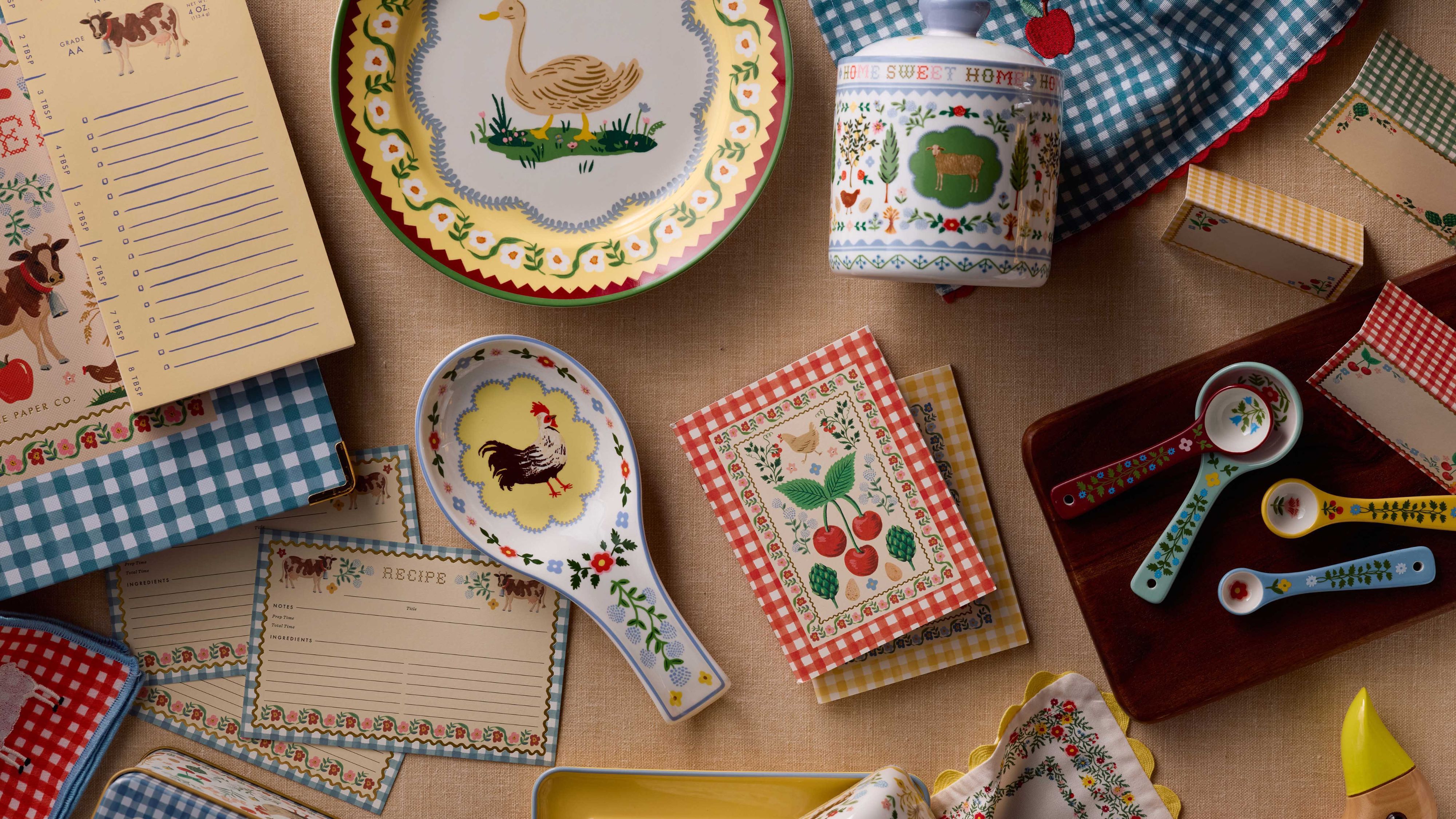 Rifle Paper Co.'s Country Home tableware and lifestyle collection, including heritage-patterned plates, spoon rests, notepads, and kitchen essentials, pictured on a wooden countertop
