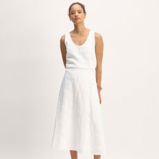 a model wears a white tank top tucked into a matching A-line midi skirt