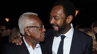 Sir Trevor McDonald and Sir Lenny Henry in dark suits share a joke at a party.