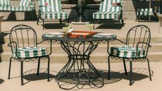 Whimsical iron outdoor bistro table and chairs, pictured in front of a row of loungers with green-and-white striped cushions