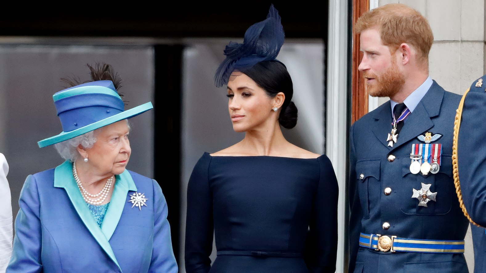 Queen Elizabeth II, Meghan, Duchess of Sussex and Prince Harry, Duke of Sussex look at each other as they watch a flypast to mark the centenary of the Royal Air Force from the balcony of Buckingham Palace on July 10, 2018