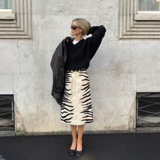 An image of an influencer wearing a zebra midi skirt, black jumper, black ballet flats and a black leather jacket.